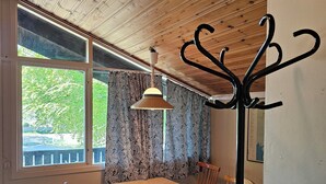 A dining area with a wooden table and chairs, a hanging light fixture, and a view through a window with patterned curtains.