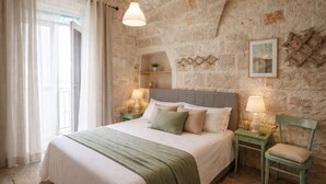Ein Schlafzimmer mit Steinsturz, einem Bett mit grüner Decke, zwei Nachttischen mit Lampen und einem Fenster mit Vorhängen.