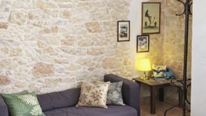 Ein Wohnzimmer mit einer Steinwand, einem violetten Sofa mit floralen Kissen, einem kleinen Tisch mit einer Lampe und einem Bilderrahmen.