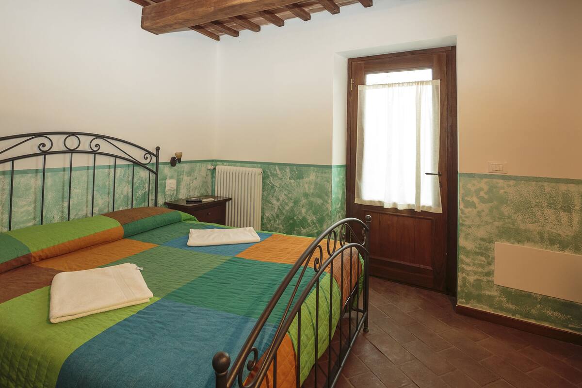 Een slaapkamer met een bed, een houten deur, een radiator en een raam met gordijn.