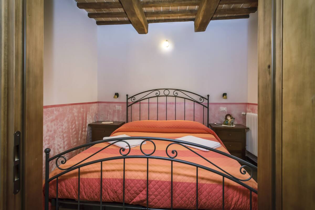 Een kamer met een bed, houten plafond en nachtkastje met lamp.