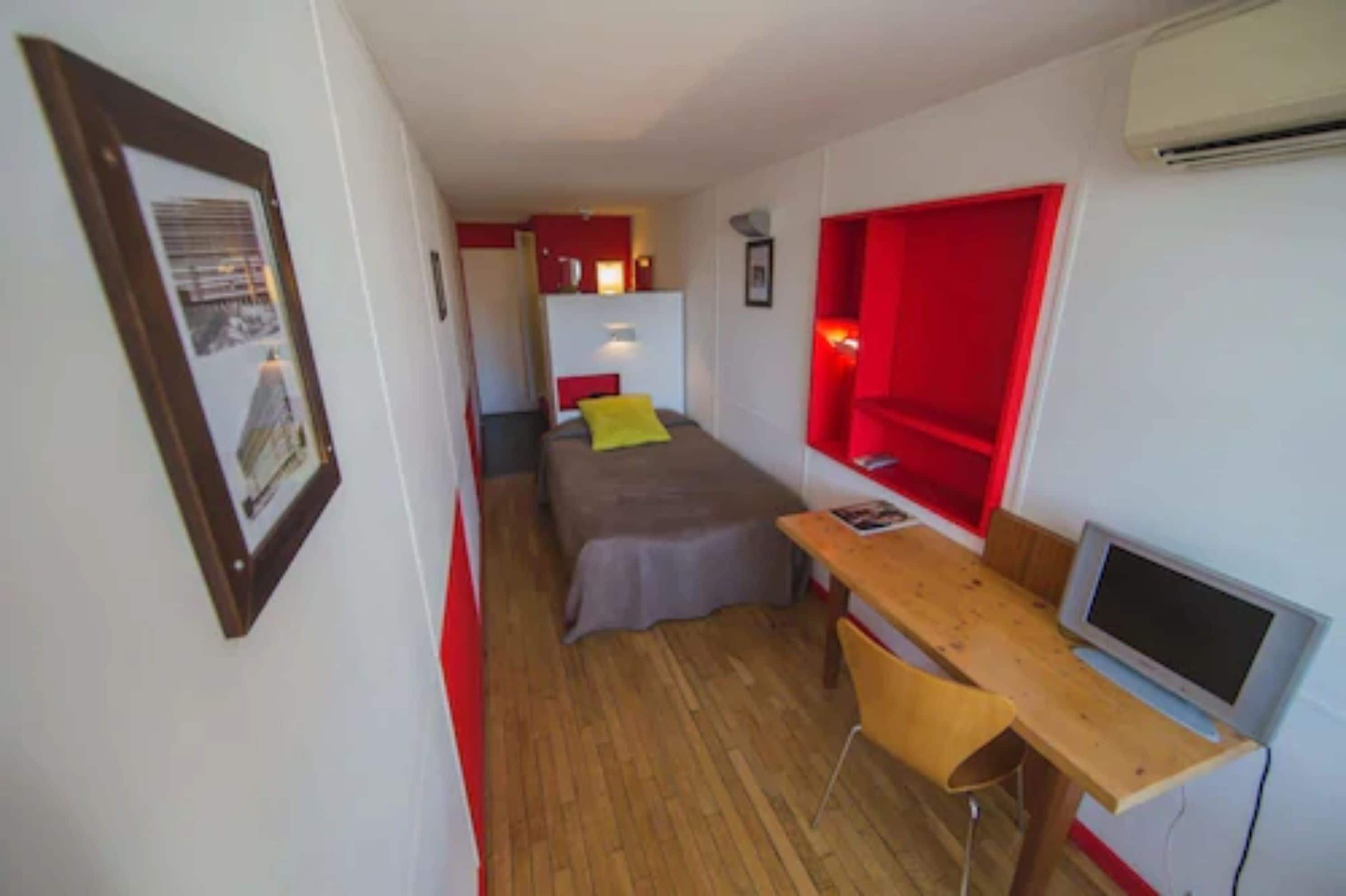 Habitació compacta amb un llit, escriptori, cadira i televisió.