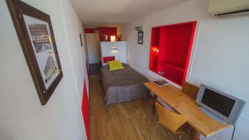 Habitació compacta amb un llit, escriptori, cadira i televisió.