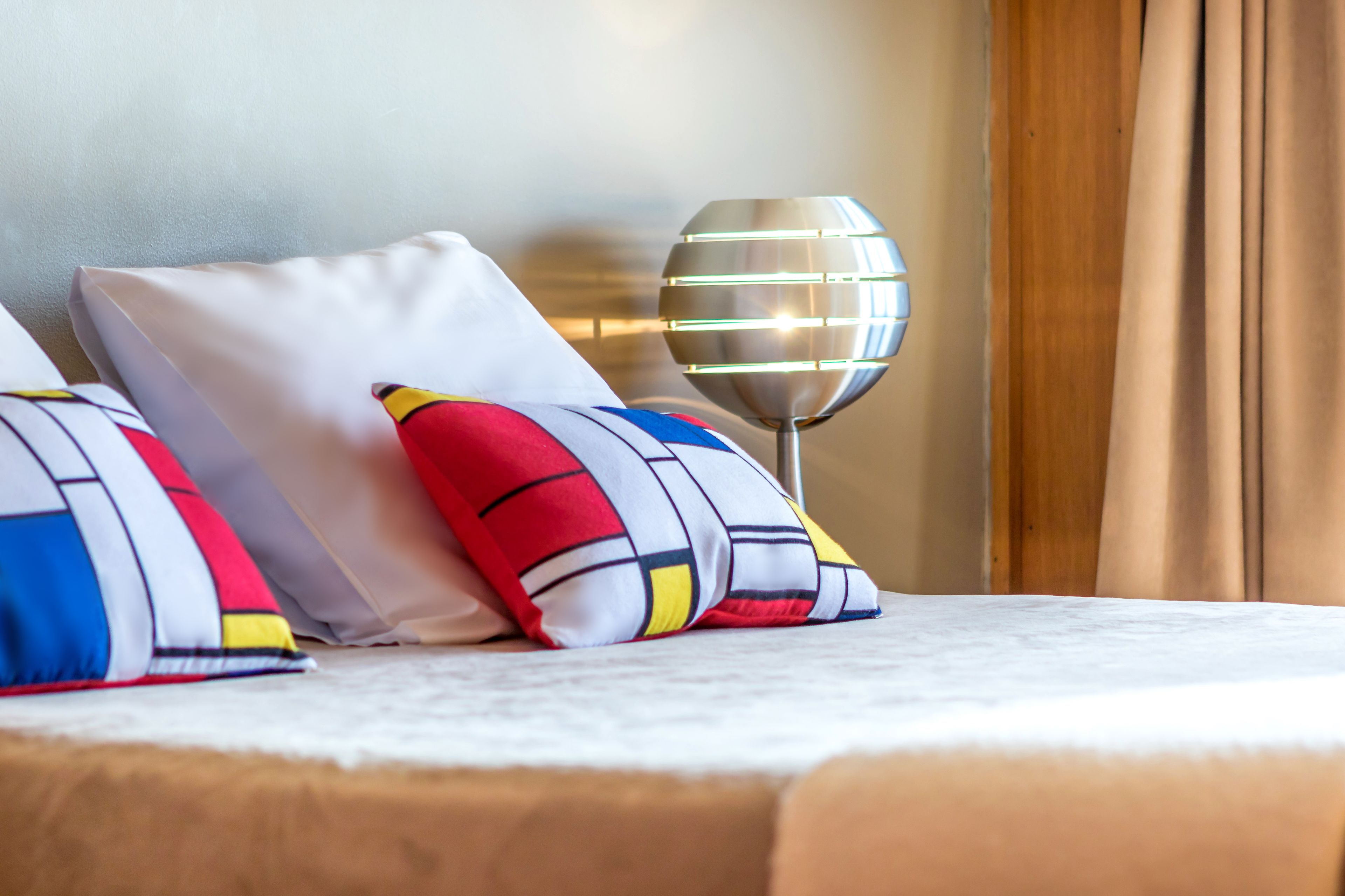 Una cama bien hecha con una colcha blanca y dos almohadas con diseño rojo, blanco y azul.