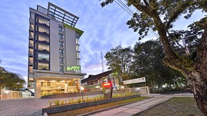 Un hotel moderno con un llamativo letrero 'WHIZ', fachada de vidrio, varios pisos y un área de entrada ajardinada.