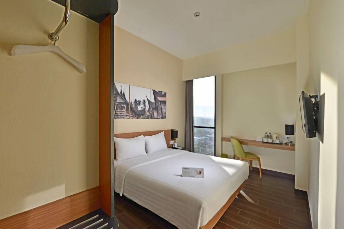 A hotel room with a large bed, a desk with a chair, a TV, and a window with a city view.