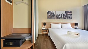 Ein Hotelzimmer mit einem Bett, einem Nachttisch, einem Schreibtisch, einem Kleiderschrank und einer Wand mit Kunstwerken.