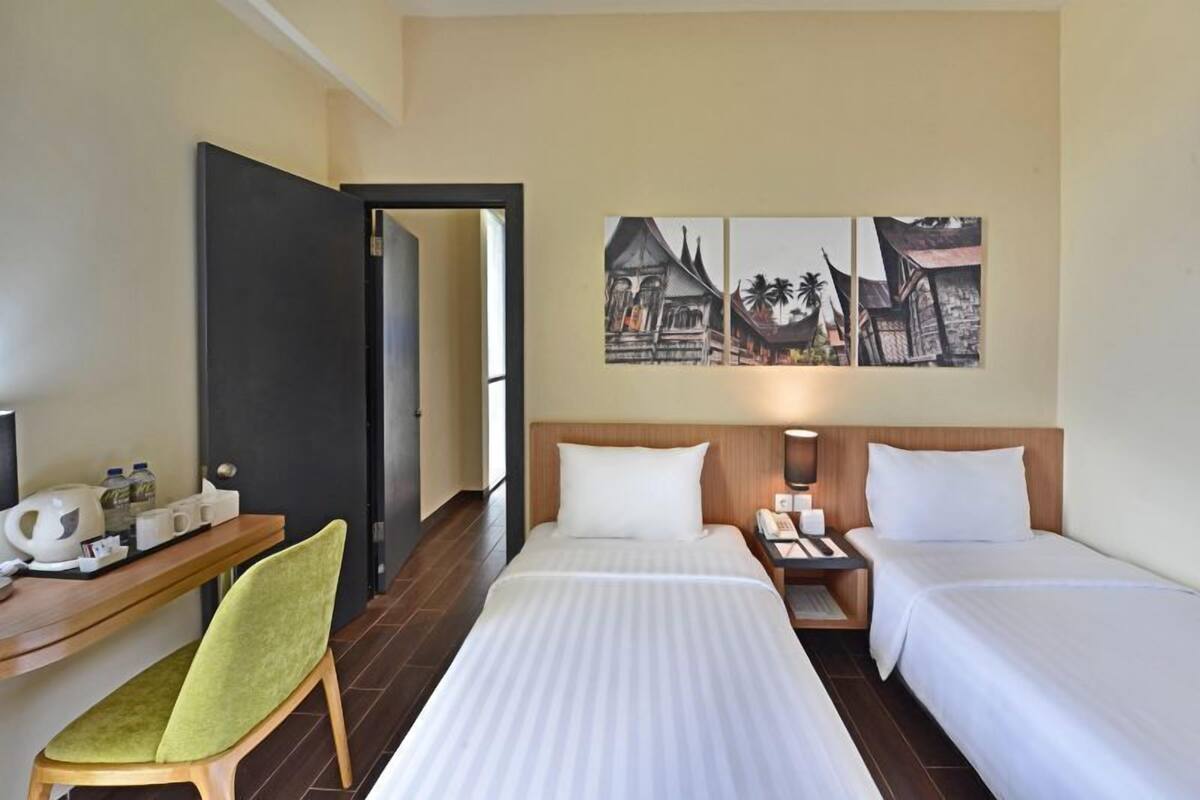 A hotel room with two beds, a desk with a chair, a nightstand with a lamp, and a wall with three framed pictures.