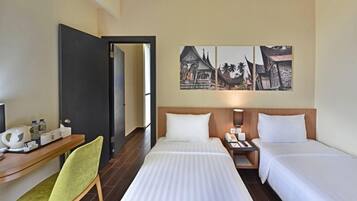 Hotelkamer met twee bedden, een bureau met stoel, een nachtkastje met lamp, en een muur met drie ingekaderde foto’s.
