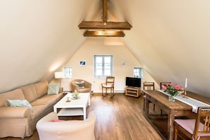 A cozy living room with a wooden ceiling, a sofa, a coffee table, a dining table with chairs, and a television. - Apartment 8 for 4 persons with beautiful lake view - Gut Grubnow Rügen (Neuenkirchen)