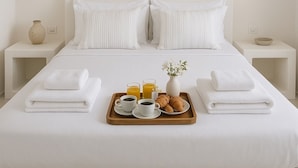 Een net opgemaakt bed met witte lakens, twee kussens, en een dienblad met ontbijtartikelen zoals croissants, koffie en sap.