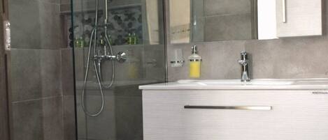 A modern bathroom with a glass-enclosed shower, a white vanity with drawers, and a large mirror above the sink.