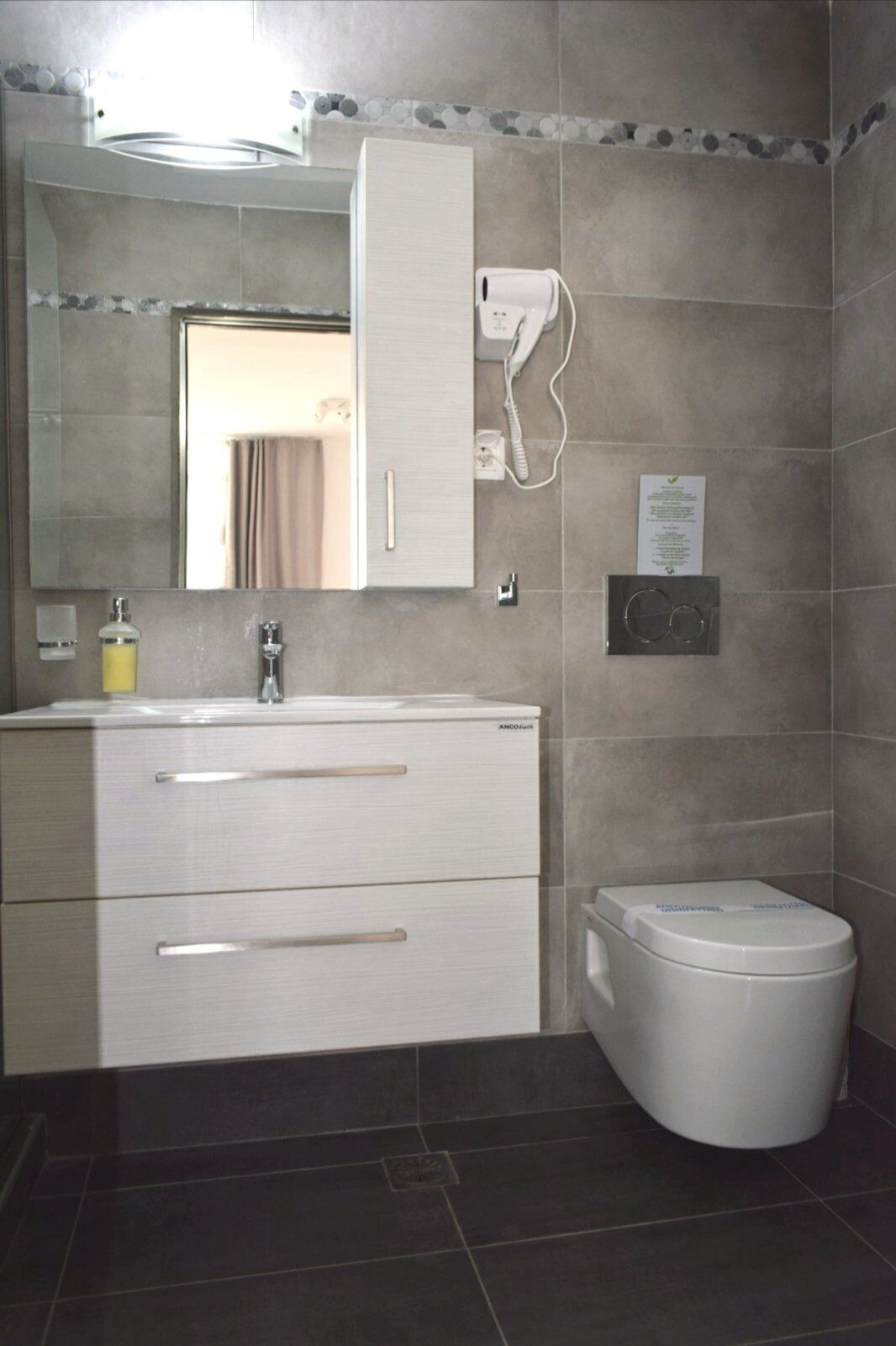 A bathroom with a white sink, mirror, and cabinet, a toilet, and a wall-mounted hairdryer.