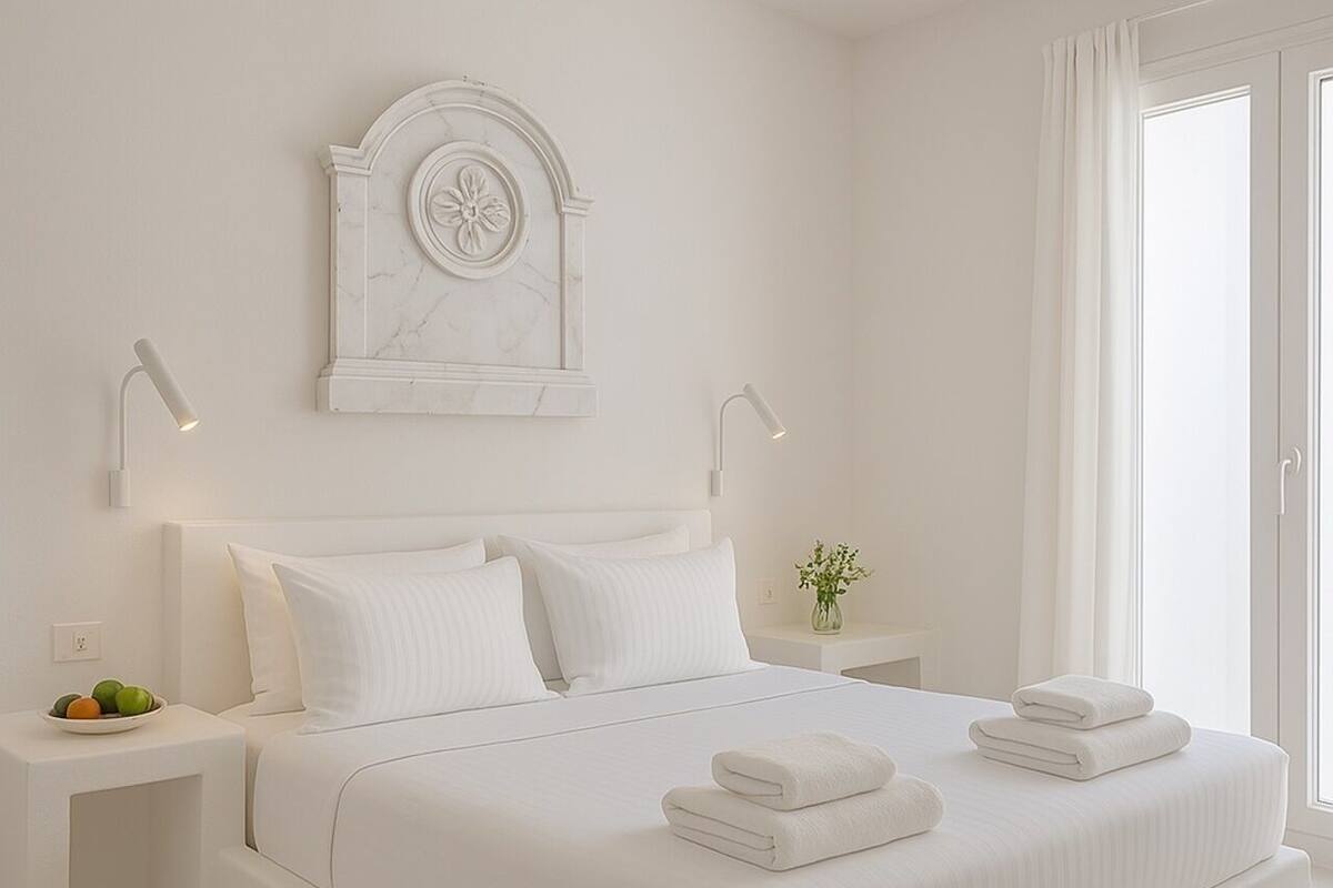 Quarto moderno com cama grande, roupa de cama branca, decoração de parede em mármore, luminárias de cabeceira e mesa de cabeceira com frutas.