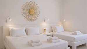 Een hotelkamer met twee bedden, wit beddengoed, wanddecoratie in de vorm van een zon en nachtlampjes.