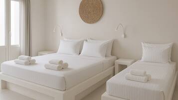 Quarto de hotel com duas camas, cada uma com roupa de cama branca e toalhas enroladas. Há uma peça de arte de parede em tear acima das camas e uma pequena mesa de cabeceira com uma luminária.