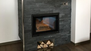 A modern fireplace with a stone facade, a firebox, and a log holder.