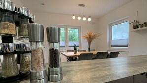 A modern kitchen with a wooden countertop, a dining table, and a window with a view of trees.