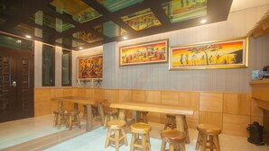 Um restaurante com mesas e banquetas de madeira, quadros nas paredes e chão de azulejos.
