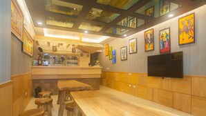 Um restaurante com mesas e bancos de madeira, uma televisão presa à parede, e obras de arte coloridas nas paredes.
