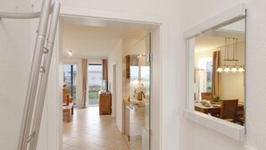 A corridor leading to a dining area with a view of the outdoors, a kitchen area with a television, and a dining table set for four. - Amazing apartment in Rechlin with sauna (Rechlin)