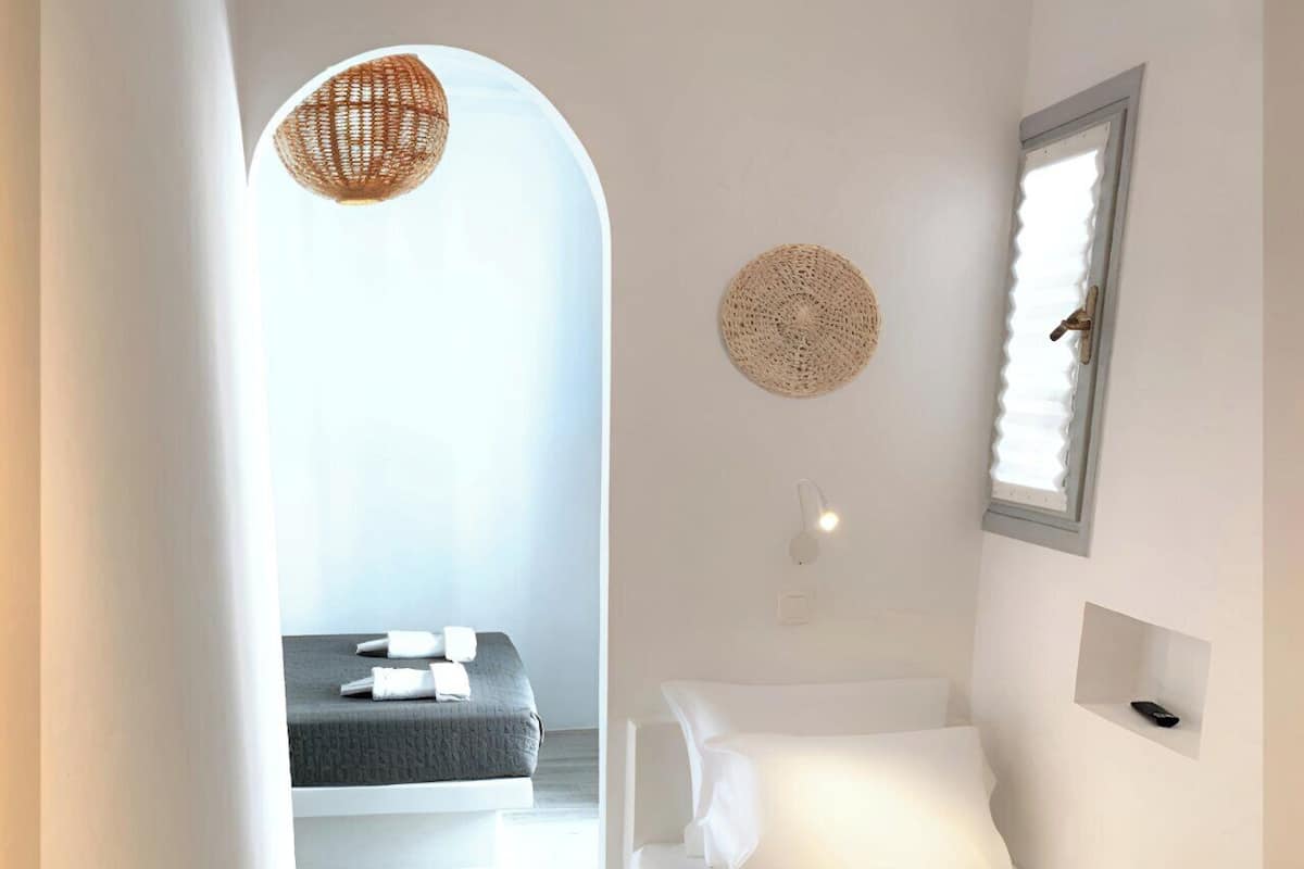 Un pasillo estrecho que conduce a un dormitorio con una cama, una mesita de noche y una lámpara de pared.