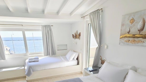 Una habitación de hotel con una cama grande, otra más pequeña, un escritorio y vistas al mar.