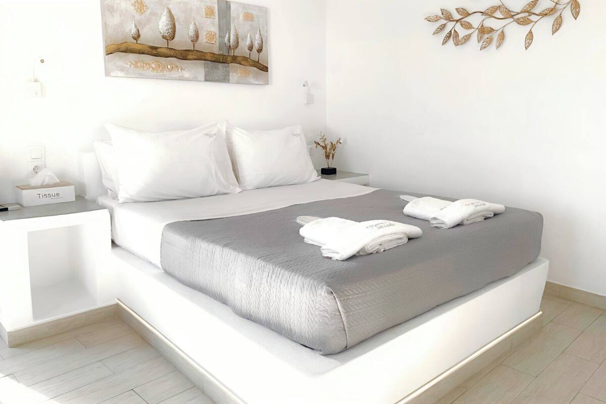 Una habitación de hotel moderna con una cama grande, ropa de cama blanca, una mesita de noche con una caja de pañuelos y una obra de arte colgada en la pared.