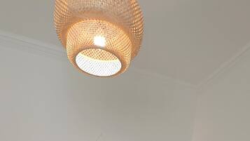 A neatly made bed with towels, a hanging macrame wall decoration, and a woven light fixture above it.