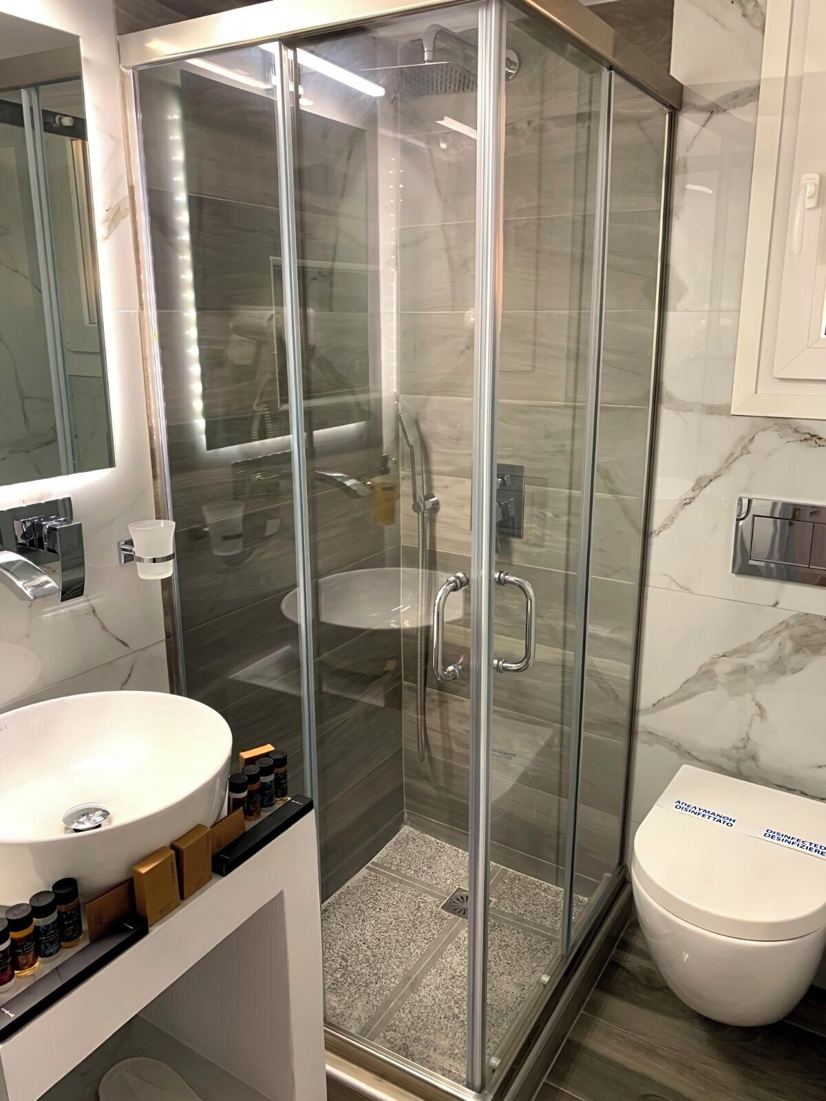 Un baño moderno con ducha de vidrio, lavamanos blanco y retrete.
