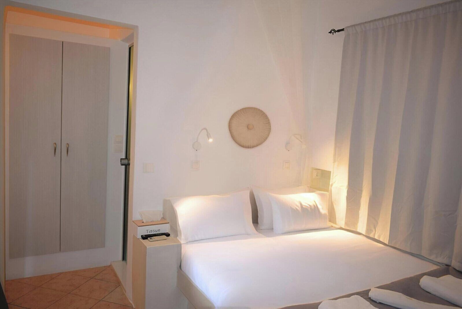 Una habitación de hotel con cama, mesita de noche, armario y cortina.