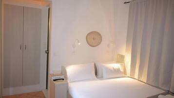 Una habitación de hotel con cama, mesita de noche, armario y cortina.