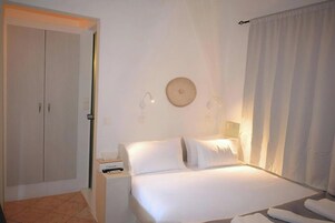 Una habitación de hotel con cama, mesita de noche, armario y cortina.