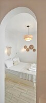 A bedroom with a bed, a hanging light fixture, wall decor, and a wooden floor.