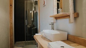 A bathroom with a wooden vanity, a white sink, a glass shower enclosure, and a mirror with a wooden shelf above it.