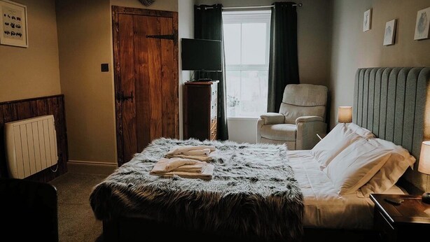 A bedroom with a large bed, a chair, a TV, and a window with curtains. - Troutbeck Inn (Penrith)