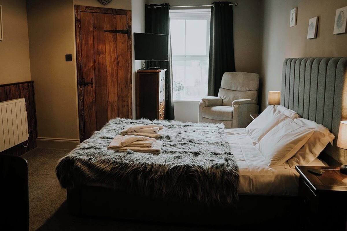 A bedroom with a large bed, a chair, a TV, and a window with curtains.