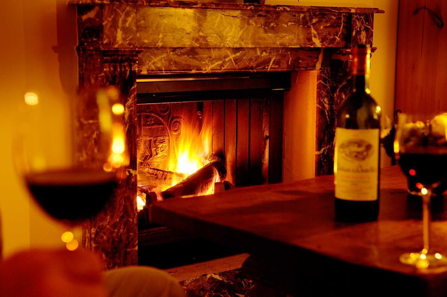 Une pièce chaleureuse avec une cheminée, une bouteille de vin et des verres sur une table.