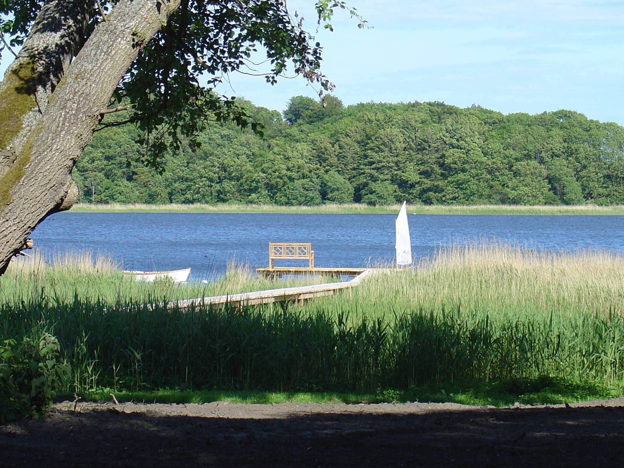 Une vue sur le lac, avec une jetée en bois, un banc et un obélisque blanc.
