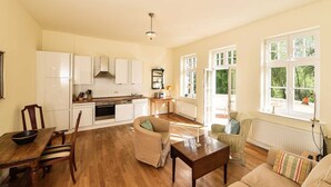 A spacious living area with a kitchen, wooden flooring, and large windows offering natural light. - Apartment 7 with lake view and large balcony - Gut Grubnow Rügen (Neuenkirchen)