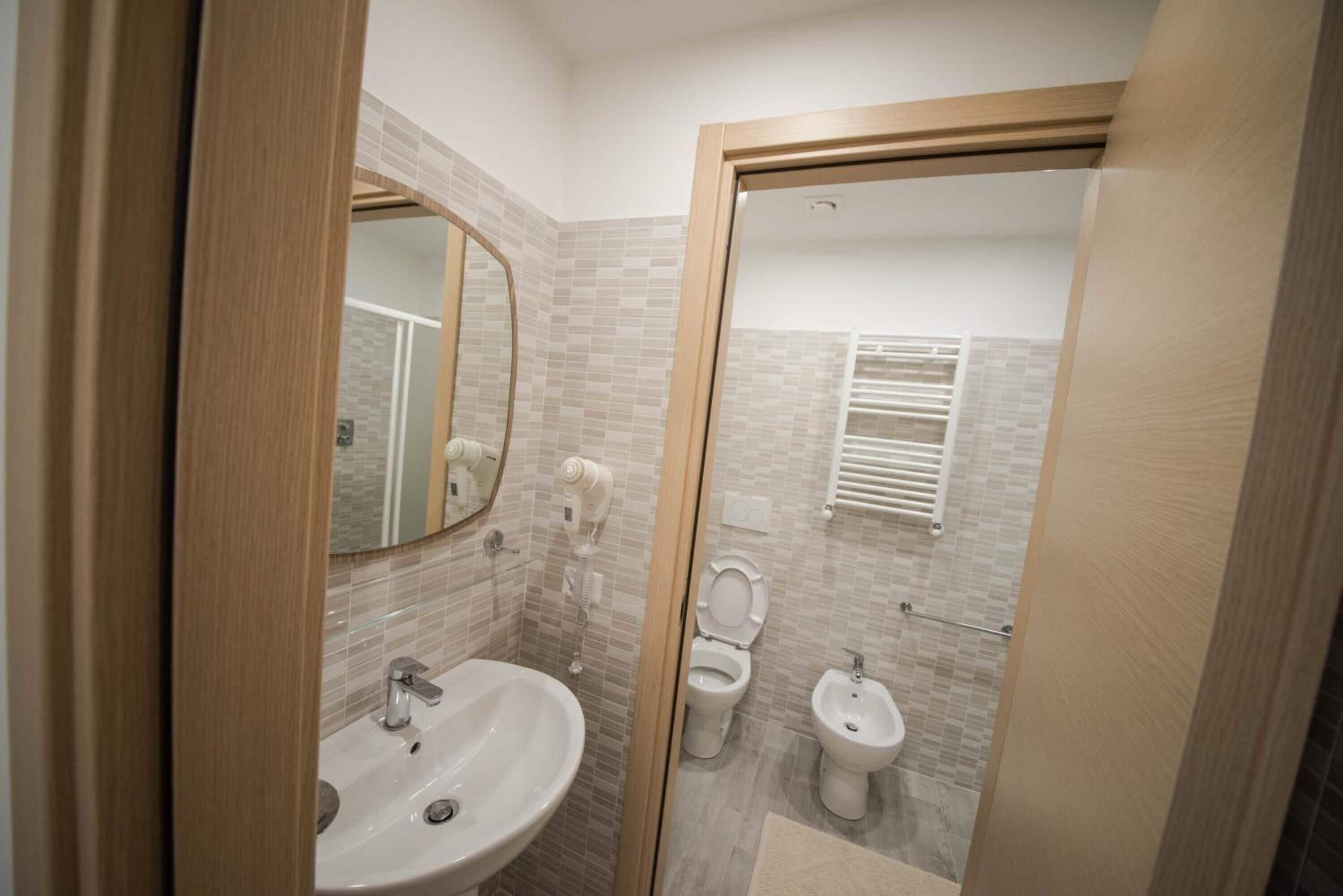 A modern bathroom with a sink, toilet, bidet, and a mirror.