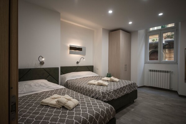 A modern hotel room with two beds, a small wall-mounted light, a radiator, and a window with a view of greenery. - 5 Terre Lodge (La Spezia)