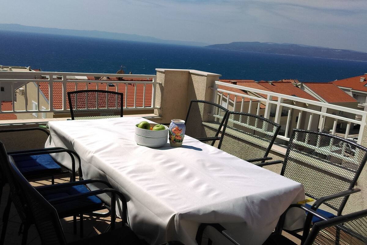 A table set on a balcony with a view of the sea and distant mountains.