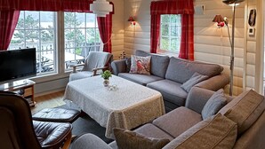 Un salon confortable avec un canapé, une table basse, un téléviseur et une vue sur l’extérieur grâce à de grandes fenêtres.