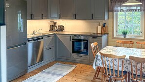 Une cuisine avec des meubles de couleur grise, un lave-vaisselle, un four et une machine à café. Il y a une fenêtre donnant sur un paysage verdoyant.