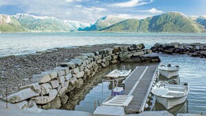 Une jetée où sont amarrés des bateaux, un mur de pierre et un lac paisible, avec des montagnes en arrière-plan.