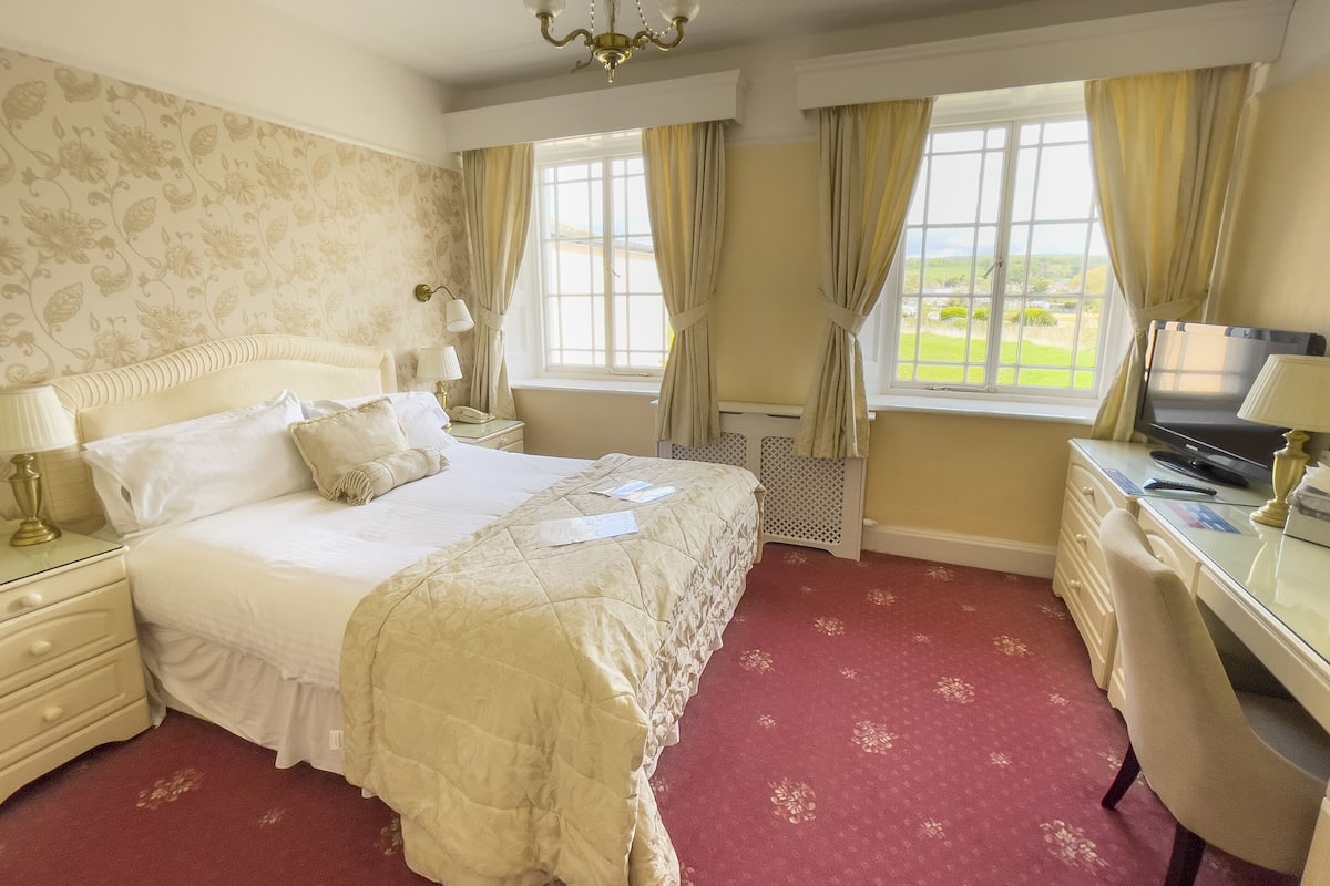 A hotel room with a large bed, a desk with a television, and a window with curtains.