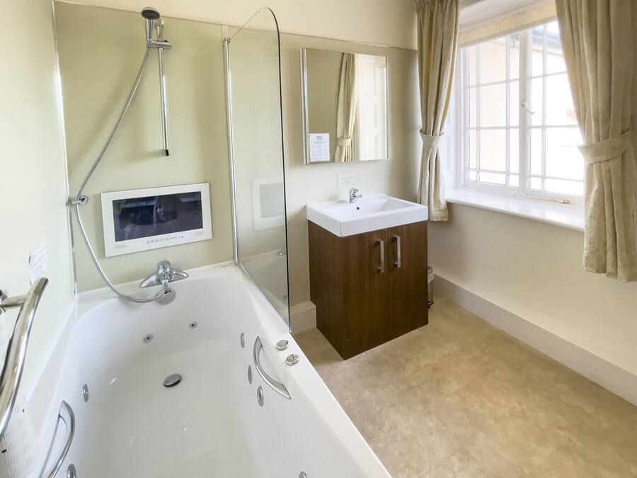 A bathroom with a bathtub, a shower, a sink, and a window with curtains.