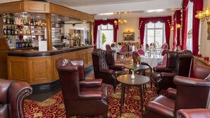A bar area with a variety of bottles and glasses, leather chairs, and a dining area with tables and chairs. - Haddon House Hotel (Bridport)