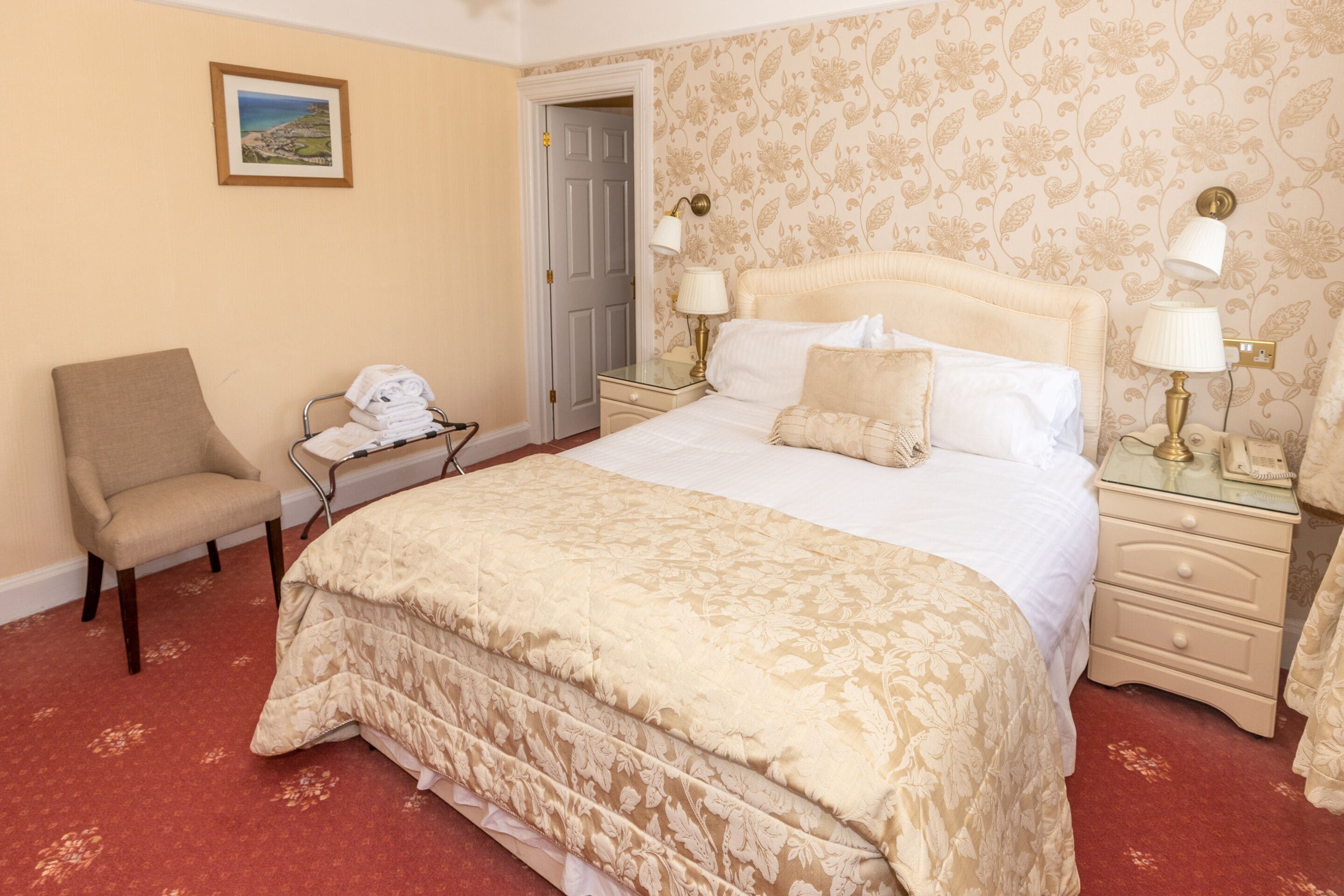 Habitación de hotel con una cama grande, una silla, un escritorio con teléfono y una puerta que da a otra habitación.